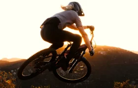 Una persona con casco conduce una bicicleta de montaña con horquillas FOX 38 2027 fuera de la carretera al atardecer, mostrando el control del enduro mientras recorren colinas bajo un cielo brillante.