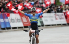 Una ciclista con el maillot de Suecia -Jenny Rissveds, oro en Río- levanta ambos brazos en señal de celebración al cruzar la línea de meta, con espectadores ondeando banderas suizas al fondo, captando su cima del mundo.