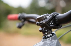 Primer plano del manillar y la potencia de una bicicleta de montaña, en el que destaca un puño ReaFlex 6.0 de un rojo intenso a la izquierda, todo ello montado en la robusta potencia Gravity 6.0, con un fondo natural desenfocado que aporta profundidad a la escena.