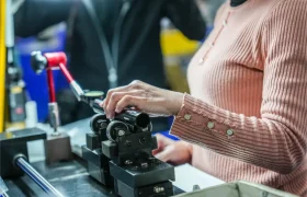 Una persona con jersey rosa maneja una máquina con pinzas metálicas que sujeta un objeto cilíndrico en un entorno industrial, dentro de la distribución oficial de equipos KS Sportmed.