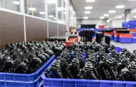 Filas de cajas azules llenas de piezas metálicas negras se organizan en el interior de unas instalaciones industriales bien iluminadas, destacando la distribución oficial de KS dentro del proceso de producción.