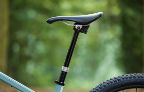 Primer plano del sillín y la tija de una bicicleta KS, con parte de la rueda trasera y el cuadro visibles, sobre un fondo verde borroso al aire libre; distribución oficial en España.