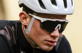 Una persona que lleva un casco de ciclista blanco, gafas de sol negras y un maillot de ciclista negro mira hacia delante mientras monta en bicicleta.