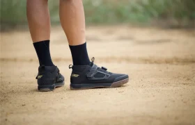 Persona con zapatillas Leatt negras y calcetines de pie en un camino de tierra, en el que sólo se ven las piernas y los pies.