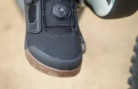 Un primer plano de una persona que lleva unas zapatillas Leatt con cierre de esfera, colocadas sobre un pedal de bicicleta, muestra el elegante diseño y las prestaciones ideales para los entusiastas del ciclismo.