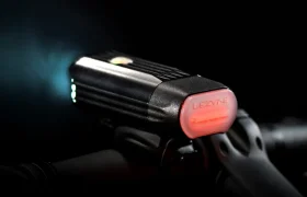 Primer plano de una luz de bicicleta Lezyne con el sistema Lezyne Radar React montado en el manillar, la luz blanca delantera encendida y una luz roja trasera visible.