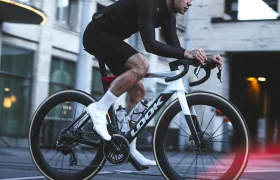 Ciclista vestido de negro que circula en una LOOK 795 Blade RS 3 por una calle de Nevers; lleva casco y calcetines blancos, con luces difuminadas en primer plano.