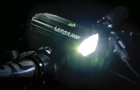 Primer plano de un faro de bicicleta Lezyne Mega Drive 2400i encendido, montado en un manillar en un entorno oscuro: algo esencial para cualquier entusiasta del Team Bike.