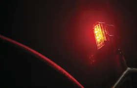 Un primer plano de una luz trasera de bicicleta LED roja Lezyne que brilla en la oscuridad, fijada al poste del asiento de una bicicleta.