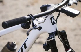 Primer plano del manillar y la horquilla de suspensión delantera de una bicicleta de montaña Pivot blanca, con un manillar integrado de carbono FSA NS SIC y un portabidón montado en el cuadro, fotografiada al aire libre.