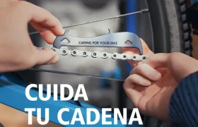 Manos que utilizan un medidor de cadena para comprobar la cadena de una bicicleta, con el texto "Cuida tu cadena" en español, perfecto para mantener tu cadena original Shimano en óptimas condiciones.