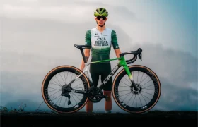 Un ciclista con el uniforme verde y blanco del equipo Caja Rural se encuentra al aire libre sujetando una bicicleta de carretera MMR Aelion SL con detalles en negro y verde, mostrando el elegante diseño de la bici asturiana.