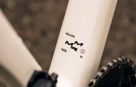Primer plano de un cuadro de bicicleta MMR Aelion SL blanco cerca de la biela, con la marca "AELION", un gráfico y la etiqueta de la talla "M". Perfecta para quienes buscan un rendimiento total en bicicleta.