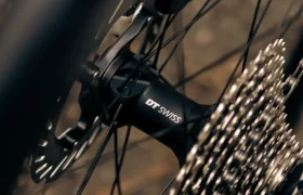 Primer plano de una rueda trasera de bicicleta que muestra el buje DT Swiss, el rotor del freno de disco y los engranajes de cassette, con parte del cuadro MMR Aelion visible al fondo, una auténtica bici asturiana.