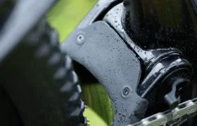Primer plano de la suspensión trasera, el neumático y la cadena de una MMR Kenta mojada, resaltando las gotas de agua en las partes metálicas, capturando la evolución total en el diseño de bicicletas de montaña.