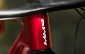 Primer plano de la sección frontal de un cuadro de bicicleta MMR Kenta rojo con "MMR" en blanco, capturando el manillar, la dirección y los cables de freno, una imagen que refleja la evolución total en el diseño de ciclismo.