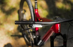 Primer plano del manillar, la palanca de freno y el cuadro de una bicicleta de montaña MMR Kenta roja, capturando la esencia de la evolución total contra un fondo exterior borroso.