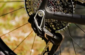 Primer plano de un desviador trasero de bicicleta, un cassette y una cadena en una rueda DT Swiss, que muestra la evolución total de la MMR Kenta contra un fondo exterior borroso.