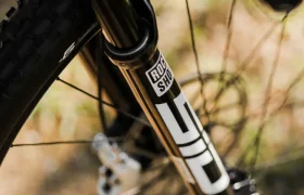 Primer plano de una horquilla de suspensión delantera de bicicleta de montaña etiquetada "RockShox SID", montada en la MMR Kenta, resaltando el neumático, los radios y parte del disco de freno: una evolución total en rendimiento y diseño.