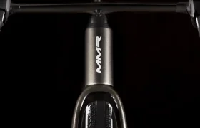 Vista de cerca del tubo de dirección de una bicicleta con el logotipo "MMR Simun", con el manillar y el neumático delantero parcialmente visibles sobre un fondo negro.