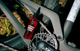 Una botella de lubricante para cadenas descansa sobre el cuadro de una bicicleta de montaña, situada cerca de la cadena y el juego de bielas de la bicicleta.