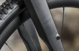 Primer plano de una horquilla y un neumático de bicicleta negros con bandas de rodadura texturizadas y la marca "Maxxis" en la pared lateral, combinados con elegantes horquillas de carbono para un mejor rendimiento.