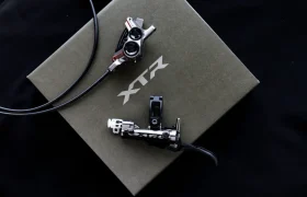 Juego de maneta y pinza de freno de disco hidráulico Shimano XTR, parte de los kits de actualización premium de Shimano, mostrados en una caja cerrada con la marca XTR sobre fondo negro.