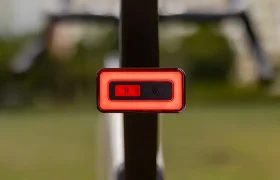 Primer plano de una luz trasera roja rectangular Sigma Nyte 70 montada en la tija del sillín de una bicicleta, con un fondo exterior difuminado.