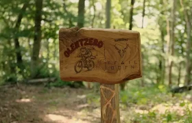 Un cartel de madera situado en la ruta de BTT «Olentzero» de Basaburua en el que se lee «Olentzero» y «Trail Born», junto con la ilustración de una figura montada en una bicicleta de montaña.