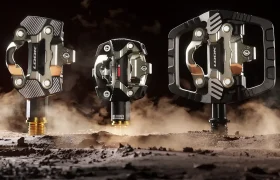 Tres pedales LOOK metálicos para Gravel se exponen en posición vertical sobre una superficie rocosa y polvorienta, con un fondo oscuro y una iluminación espectacular, para destacar su lugar en el ecosistema de pedales.