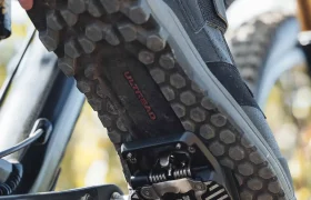 Primer plano de una zapatilla de bicicleta de montaña con suela texturizada acoplada a unos pedales Shimano DEORE XT Trail en una bicicleta.