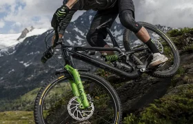 Un ciclista, que lleva casco y guantes, desciende en una bicicleta de montaña equipada con neumáticos Pirelli Scorpion MTB por una pendiente empinada y rocosa, con las montañas y las nubes como telón de fondo.