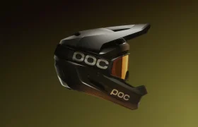 Un casco integral de descenso POC de color negro mate con visera y gafas de sol de cristales anaranjados, mostrado de perfil sobre un fondo verde oliva degradado: una elegante protección para ciclistas exigentes.