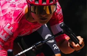 Un ciclista con casco ventilado rosa y maillot a juego monta en bicicleta al aire libre, inclinado hacia delante en posición aerodinámica.