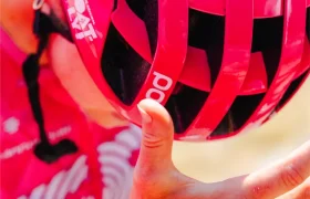 Un ciclista ataviado con un casco ventilado de color rosa chillón y un maillot a juego se seca el sudor de la frente con la mano durante un paseo.