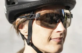 Una persona con un casco de ciclista negro casco ligero POC, gafas de sol y un maillot gris de ciclista, de frente y a plena luz del sol.