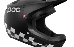 Casco integral negro Coron Air con un patrón de cuadros blancos a lo largo del borde inferior, logotipo "POC" en el lateral, acento circular rojo cerca de la zona de las orejas, ideal para pilotos como Robin Goomes. Combina perfectamente con las gafas Ora.