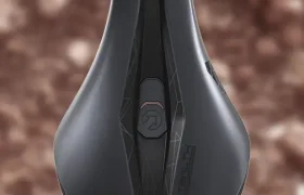 Un asiento de bicicleta ergonómico de color negro con un diseño geométrico y una marca, sobre un fondo marrón borroso.