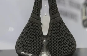 Un sillín de bicicleta ergonómico Prologo Scratch M5 PAS 3DMSS negro con un patrón de panal de abeja se muestra en posición vertical sobre una superficie reflectante.