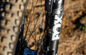 Primer plano de una rueda delantera de bicicleta de montaña con una potente horquilla de suspensión Fox 36 y componentes Bosch Performance Line CX, colocada en un sendero de arena.
