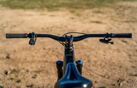 Vista en primer plano del manillar, los mandos y la horquilla delantera de una bicicleta propulsada por la potente Bosch Performance Line CX, con un camino de tierra y una zona de hierba al fondo.