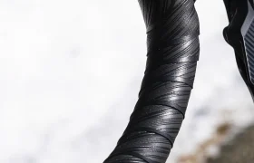 Primer plano de un manillar negro de bicicleta de carretera forrado con la cinta de manillar Silca Nastro Cuscino, una cinta texturizada diseñada para ofrecer mayor comodidad, fotografiado al aire libre junto a un suelo cubierto de nieve y una superficie de asfalto.