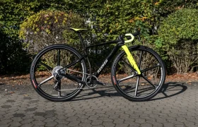 Bicicleta de gravel RAYMON con cuadro negro, horquilla delantera y cinta de manillar amarillas, y ruedas con radios negros.