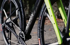 Primer plano de un cuadro negro de bicicleta de grava RAYMON con horquilla delantera de color verde brillante y neumáticos Vittoria con banda de rodadura rugosa.