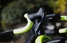 Primer plano de un manillar de bicicleta de grava RAYMON con cinta de color amarillo brillante y una palanca de cambios negra.