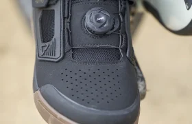 Primer plano de una zapatilla de ciclismo Leatt con sistema de cierre de dial y correa de velcro, llevada por una persona sobre un pedal de bicicleta de montaña.