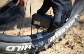 Una mano enguantada utiliza un manómetro digital Trek Air Rush para medir la presión de aire de un neumático de bicicleta de montaña al aire libre.