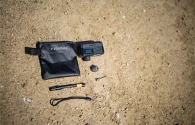 Un manómetro digital para neumáticos, una bolsa TREK negra, un adaptador de válvula, un cordón y una herramienta Trek Air Rush para inflado de ruedas están colocados sobre el suelo arenoso.