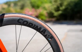 Primer plano de una rueda de bicicleta con llanta de carbono Corima 45R y neumático de flanco color canela, mostrando ligereza y rendimiento, sobre un fondo borroso al aire libre.