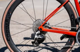 Primer plano de la rueda trasera de una bicicleta roja con llanta de carbono Ruedas Corima 45R, cubierta de pared de color tostado y cassette de cambio visible, que muestra ligereza y rendimiento en una superficie pavimentada al aire libre.